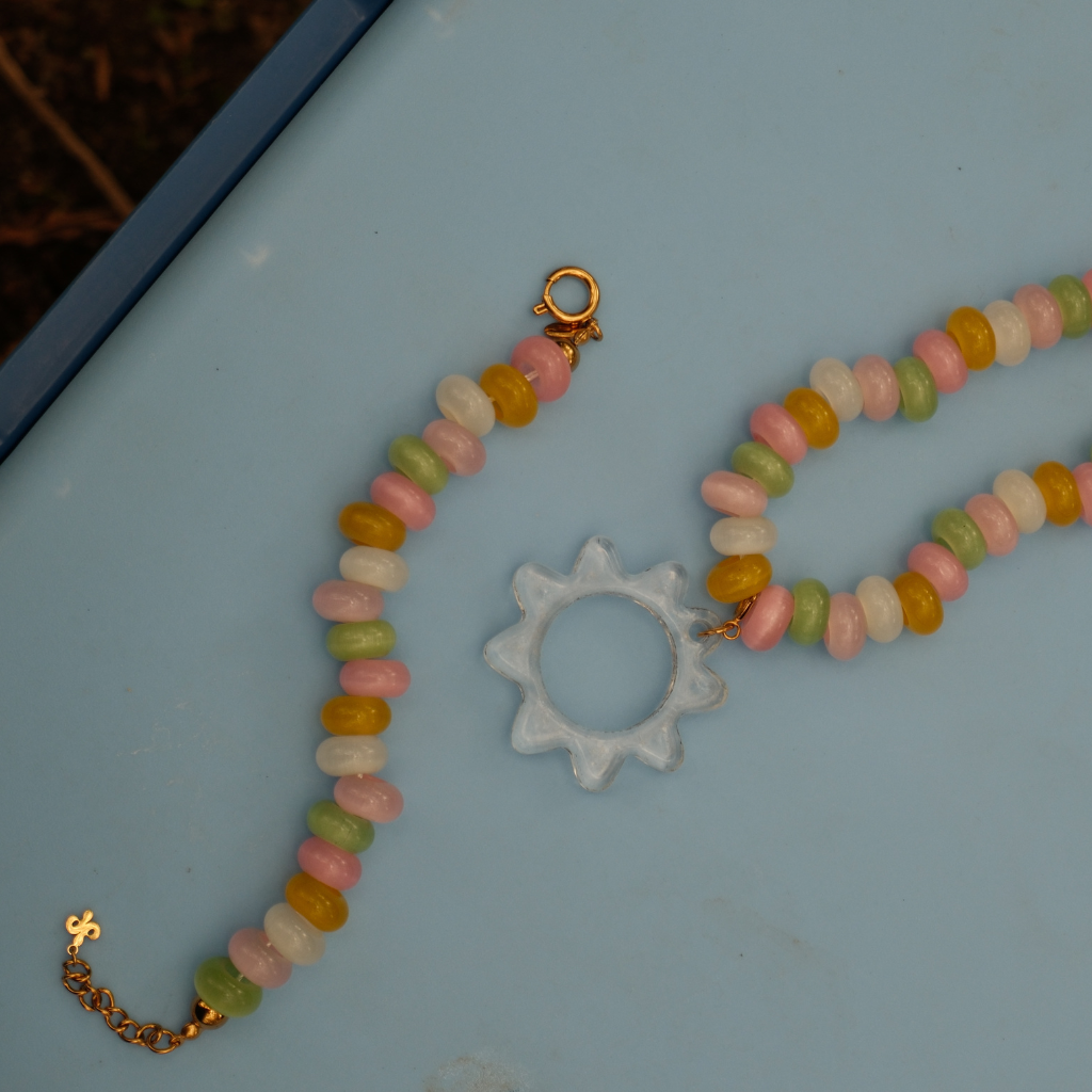 A detailed shot of the Transparent Sunray Pendant showing the glass details together with the candy stone bracelet and necklace, styled on a cooler box.